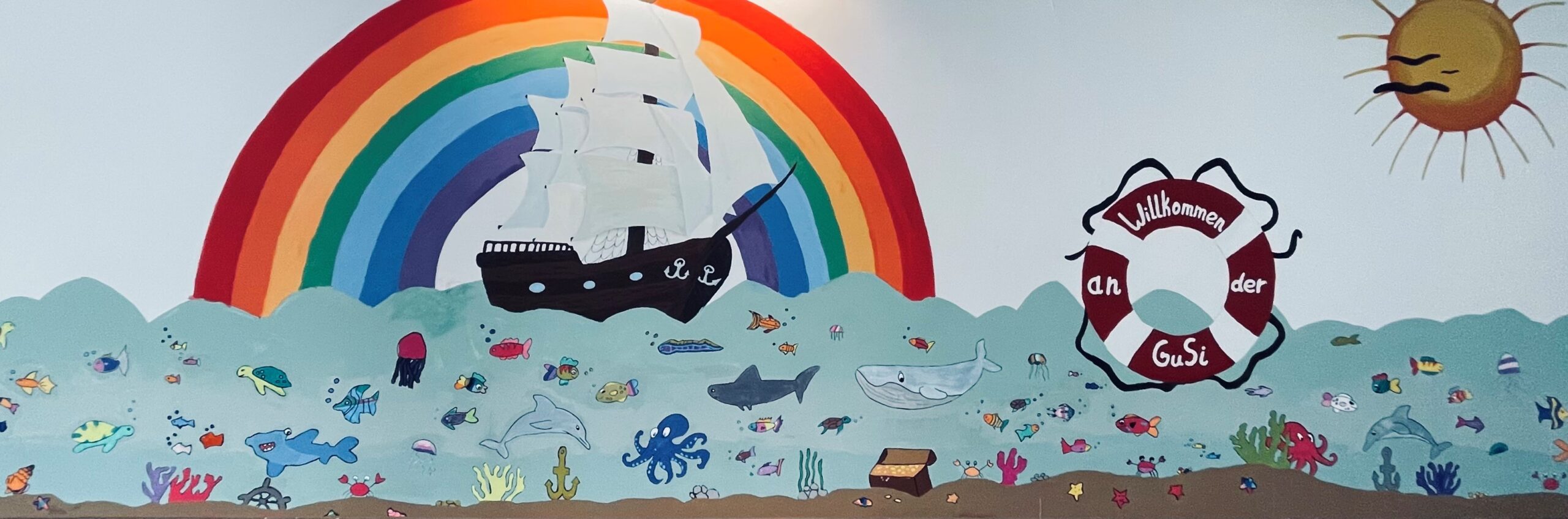Gustav-Sieber-Schule Bild im Eingangsbereich mit einem großen Segelschiff und vielen kleinen und unterschiedlichen Fischen im Wasser
